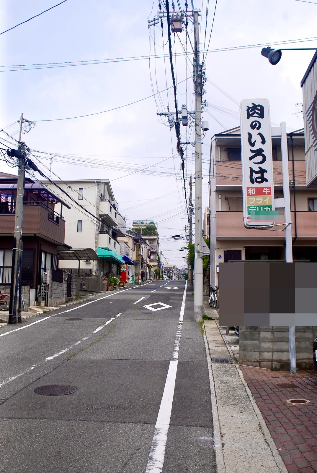 「肉のいろは」の縦看板の先に、まっすぐ続く坂道