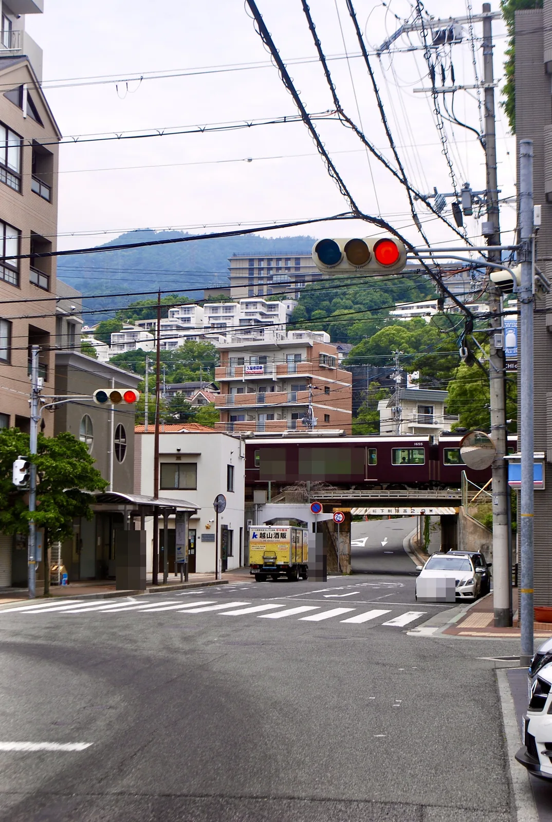 山並みとマンションを背に、阪急電車が鉄橋を渡る交差点