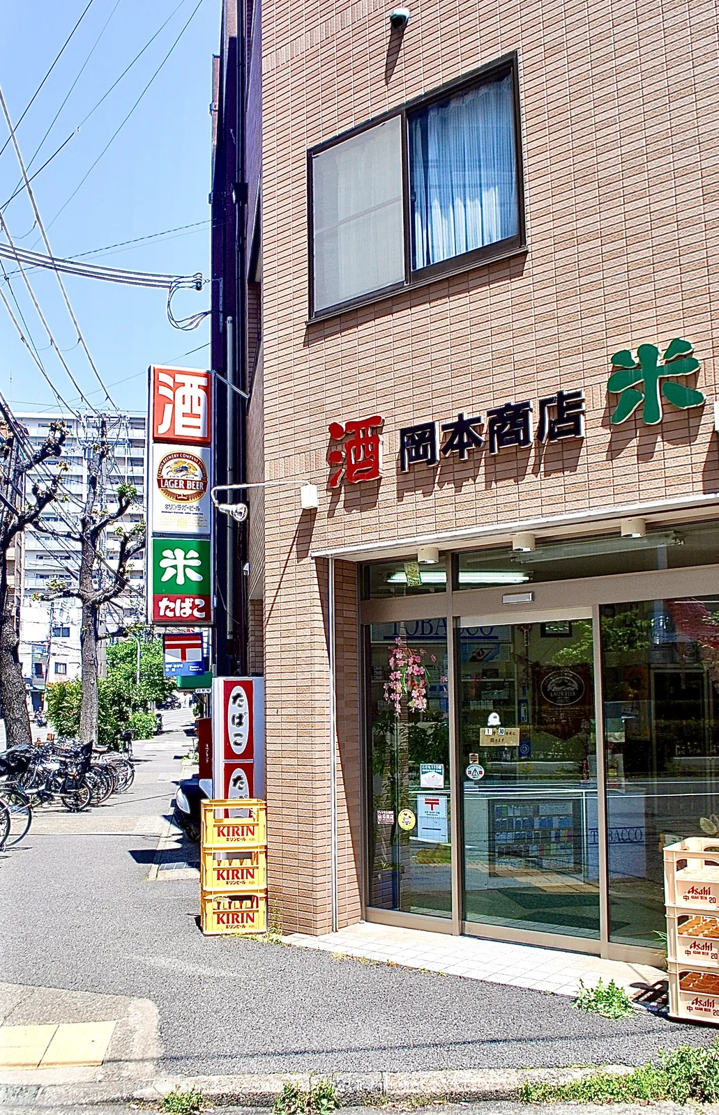 「酒」「米」「たばこ」の看板と、ビールケースが並ぶ店先