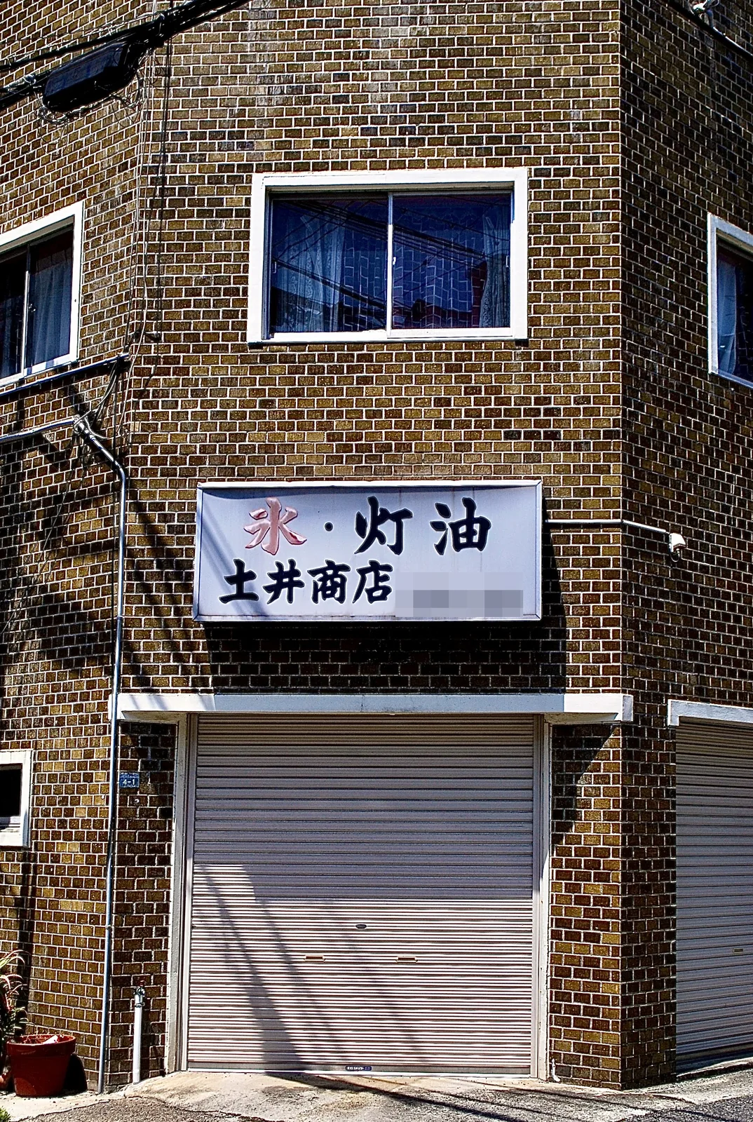 茶色いタイルの角の建物に、「氷・灯油」の看板が残る商店