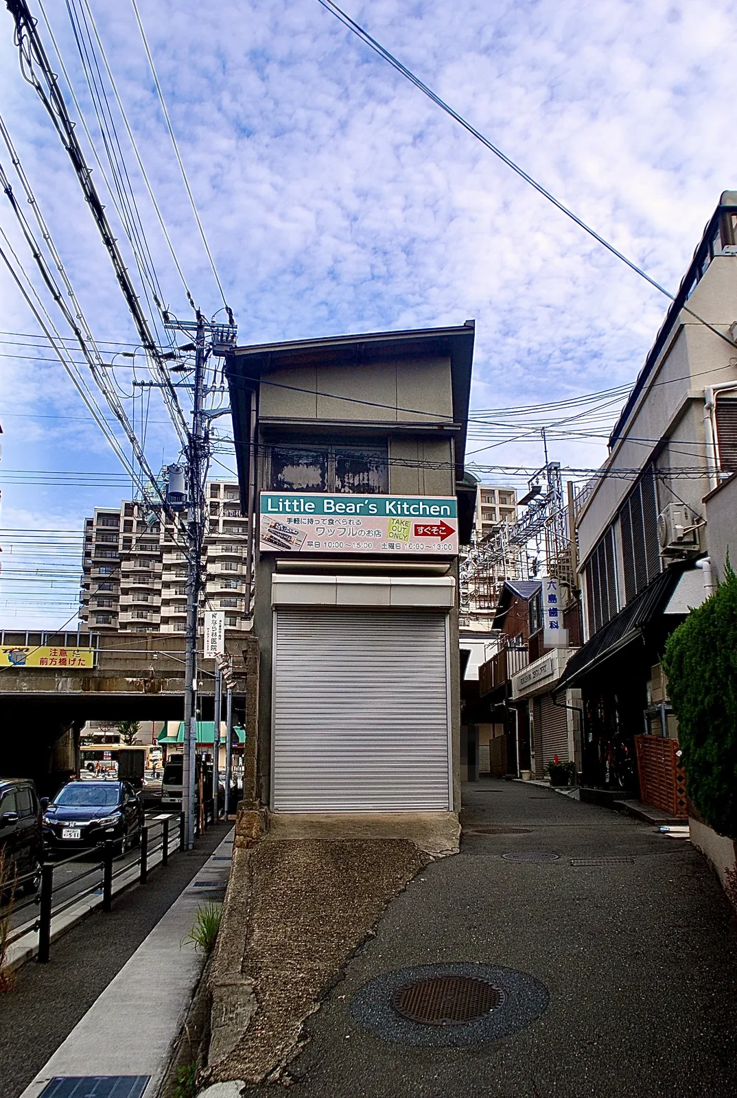 シャッターの小さな建物の脇から、看板の並ぶ路地へ続く風景
