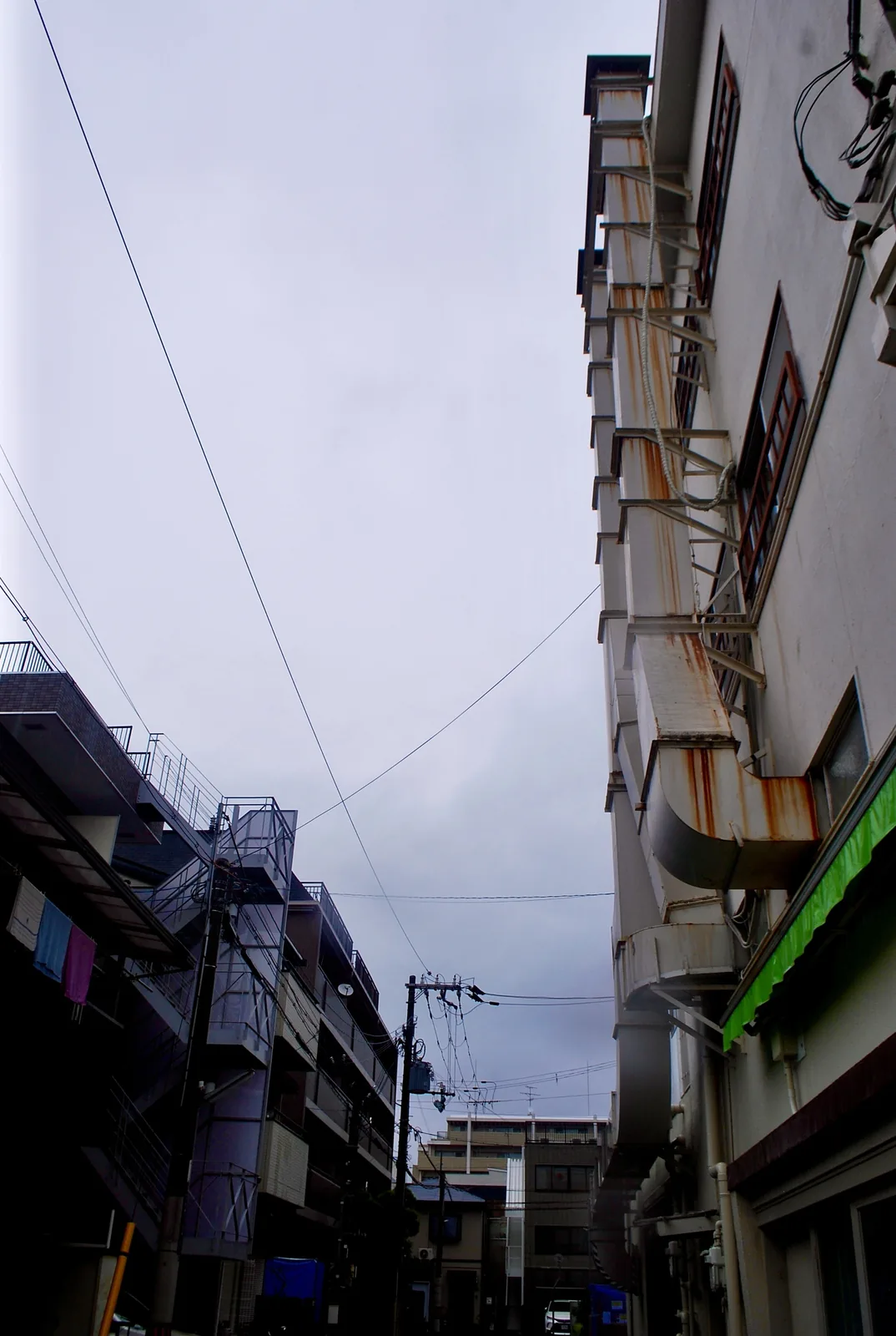 雨の日の空の下、ビルの外階段とダクトを見上げる風景