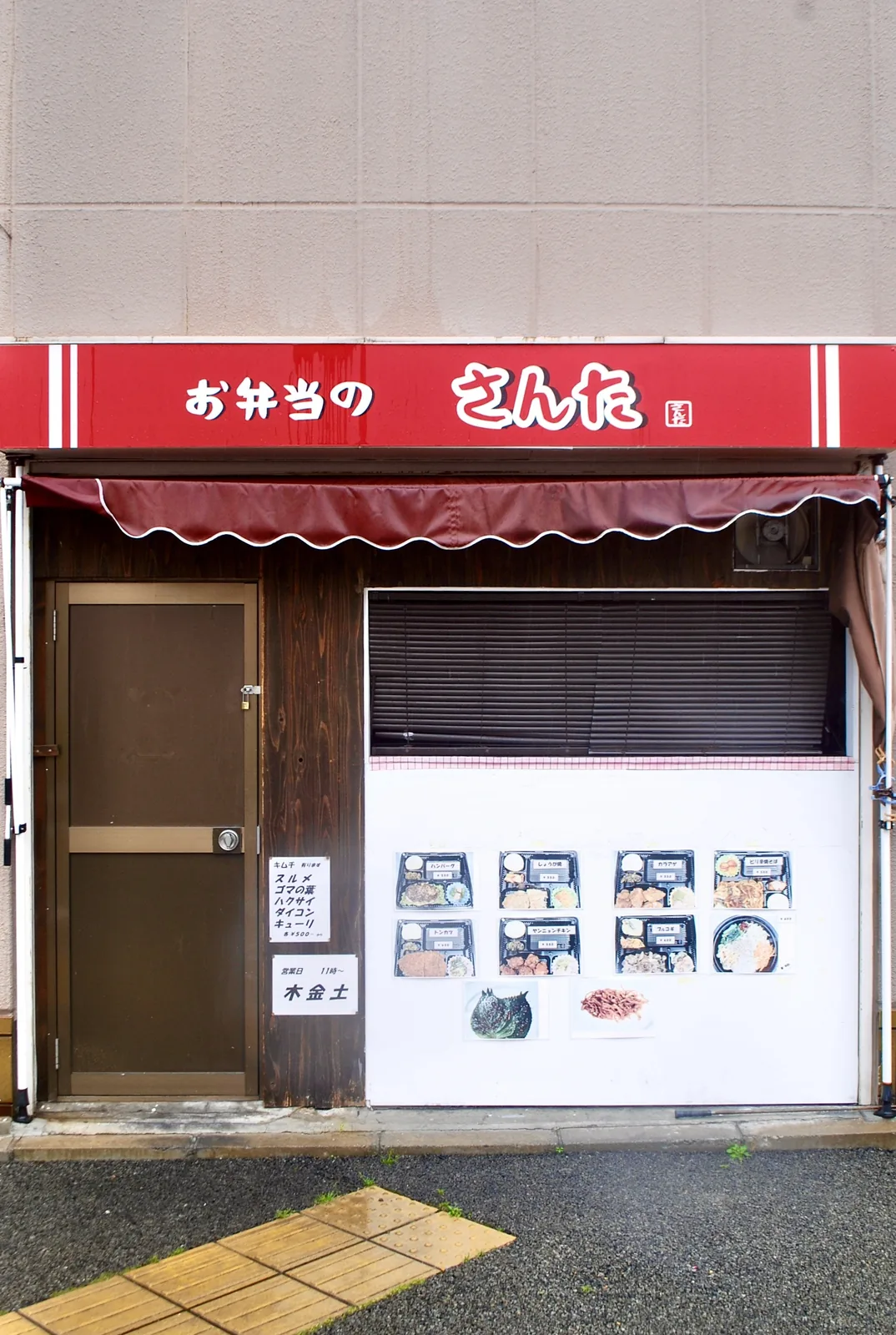 弁当の写真が並ぶ白い壁と、えんじ色の日よけ