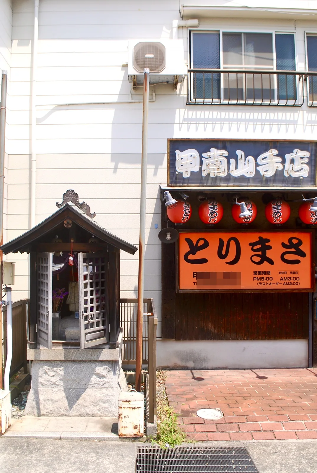 道ばたの小さなお堂と、赤い提灯が並ぶ焼鳥の店