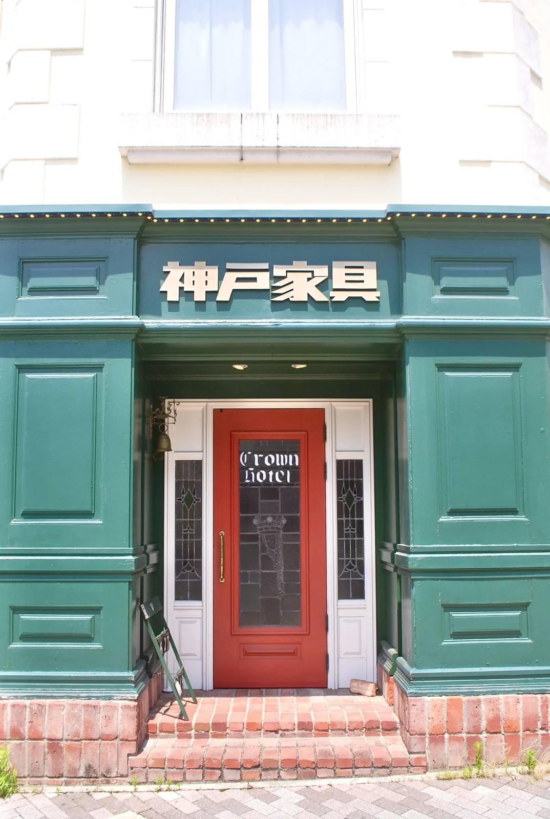 緑の壁と白い柱、赤い扉が目を引く洋風の家具店の入口