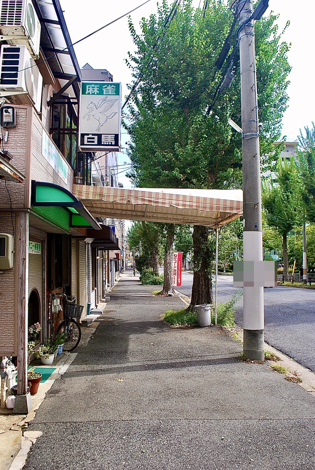 しましまの日よけと並木の下、まっすぐ続く大通りの歩道