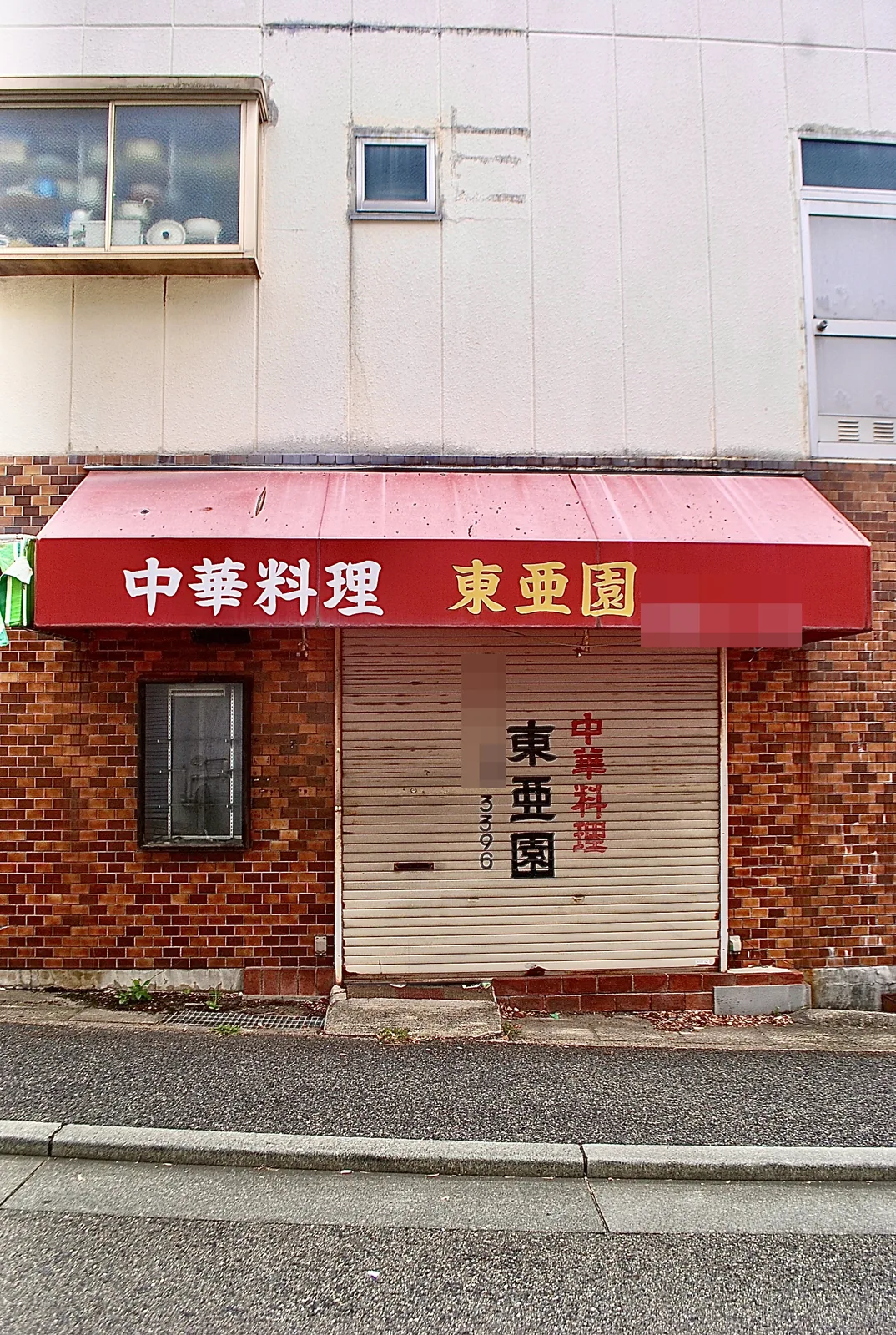 赤い日よけに「中華料理 東亜園」の文字がある、レンガ張りの店