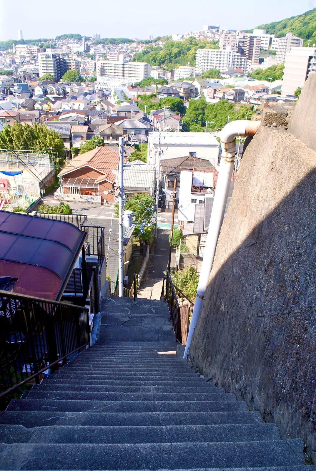 高い壁に沿って下る石段の先に、町並みと山が広がる風景