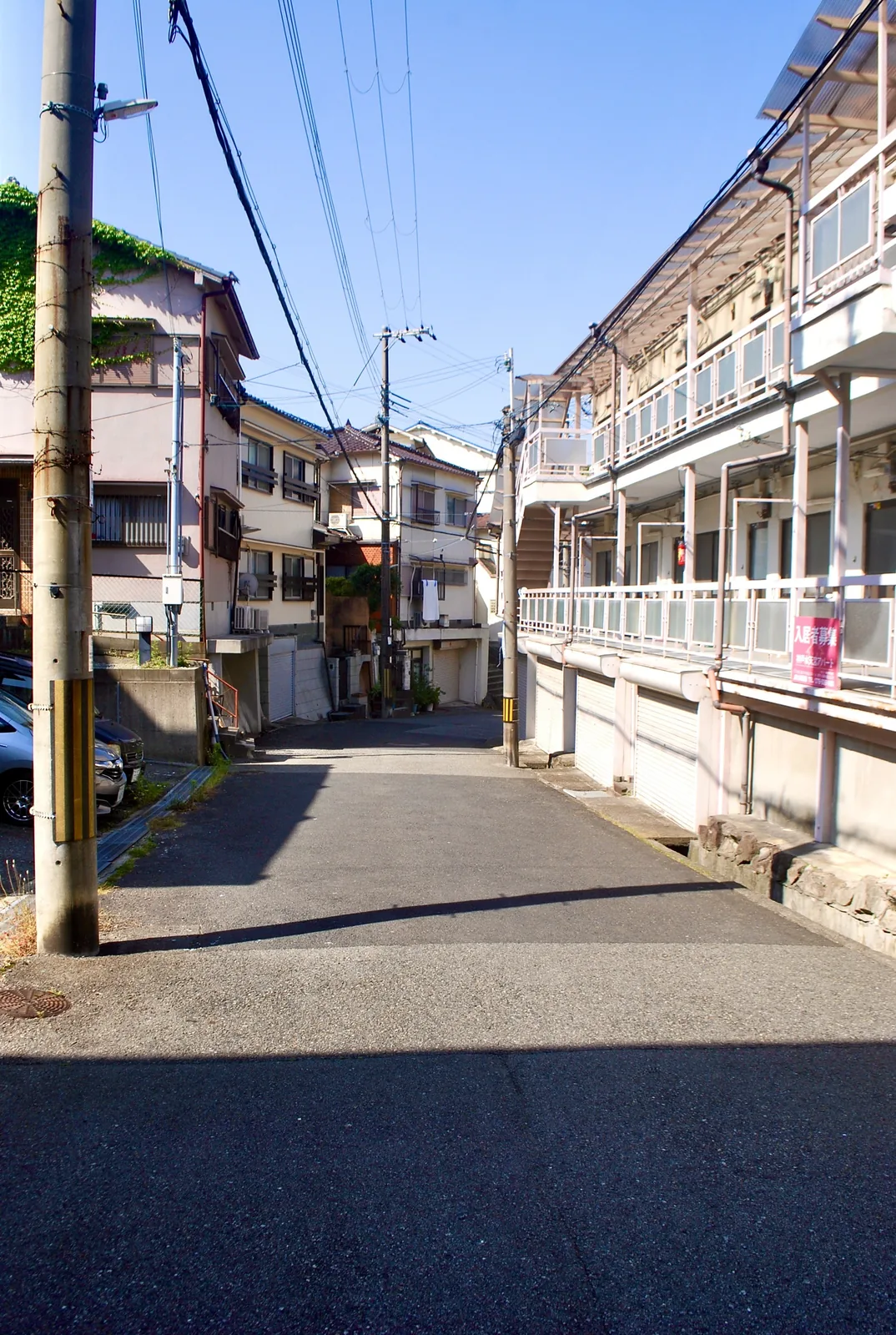 古いアパートと電柱が並ぶ、静かな住宅街の通り