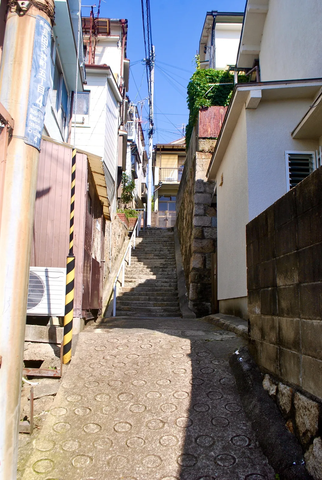 丸い滑り止めの模様の坂の先に、石段が続く路地