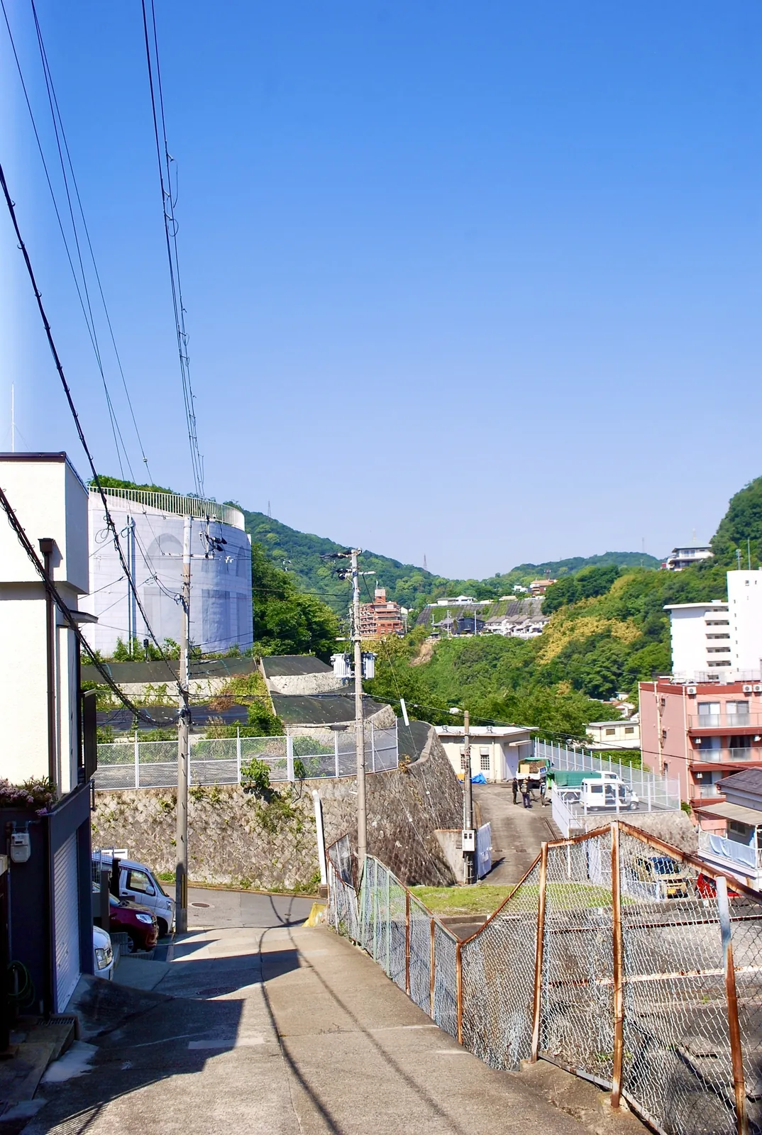 フェンス沿いの坂の上から、緑の山並みを望む風景