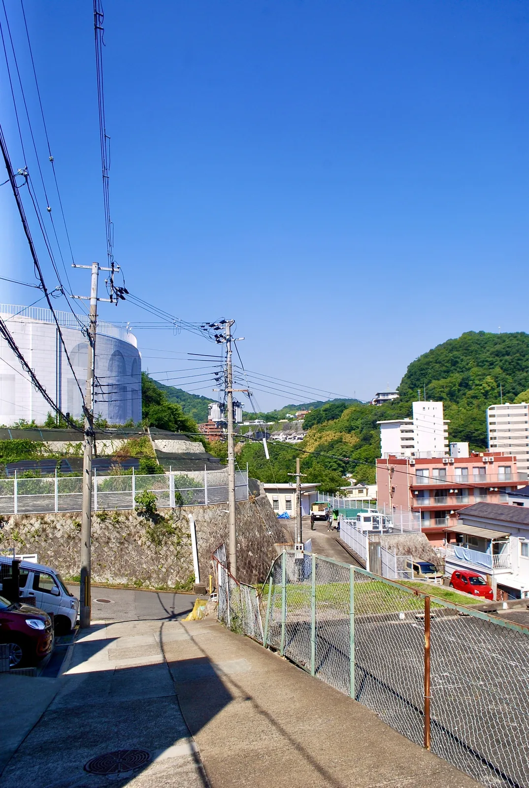 電線の張られた坂道の先に、山と町並みが広がる風景