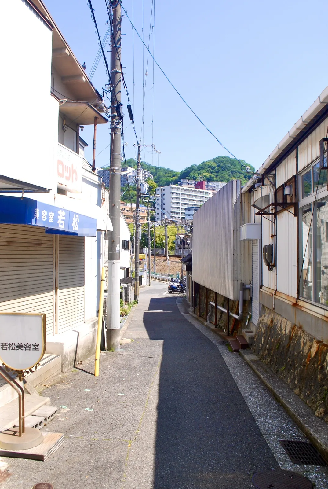 青い日よけの美容室の脇から、線路の方へ続く細い道