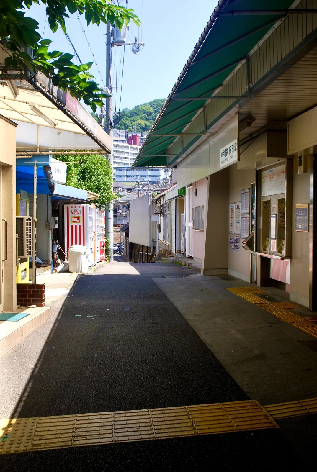 駅舎と商店のあいだの、日よけのかかる駅前の通り