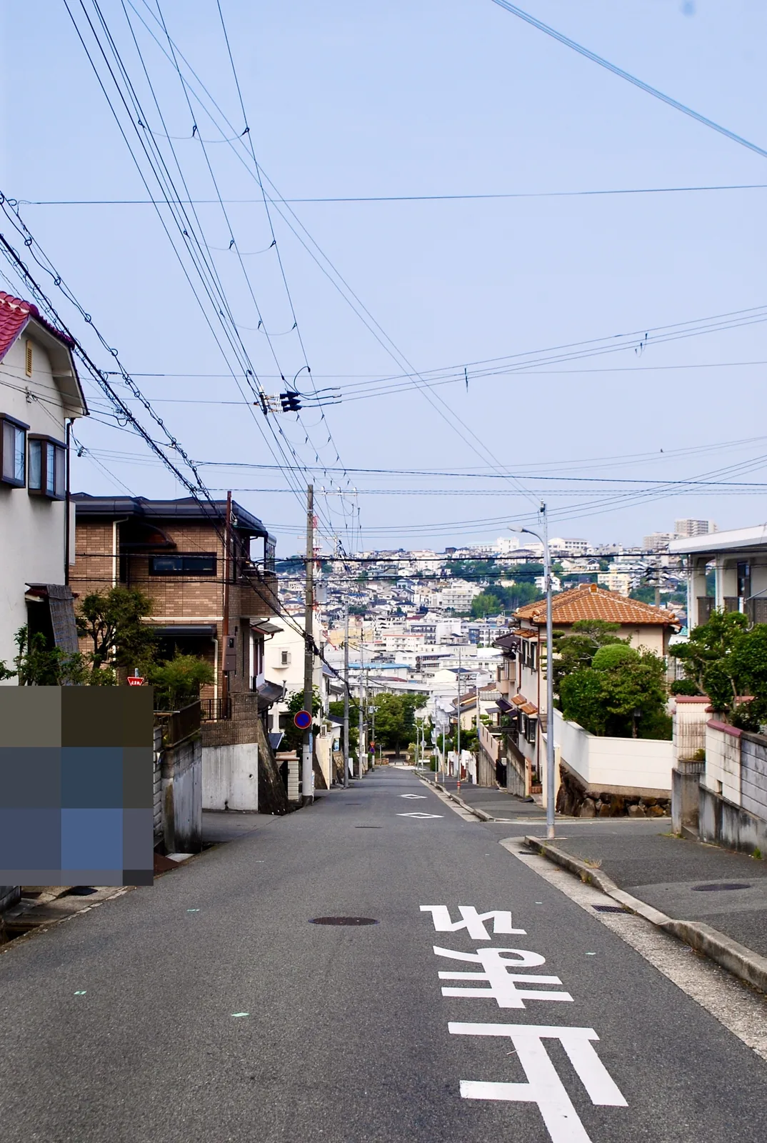 電柱と家々のあいだを、遠くの街並みへまっすぐ下る坂道