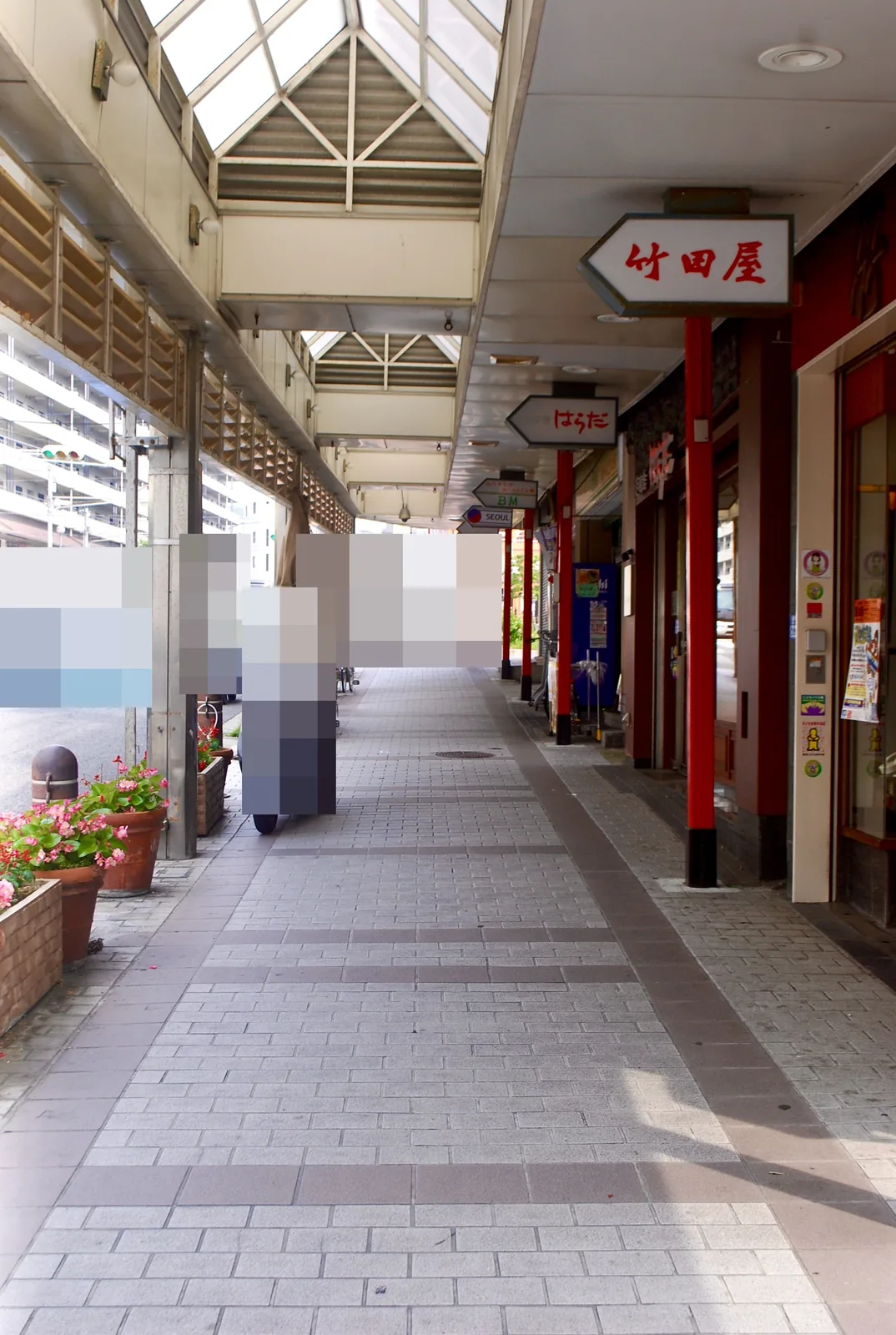 赤い柱と矢印形の看板が並ぶ、屋根つきの商店街の歩道