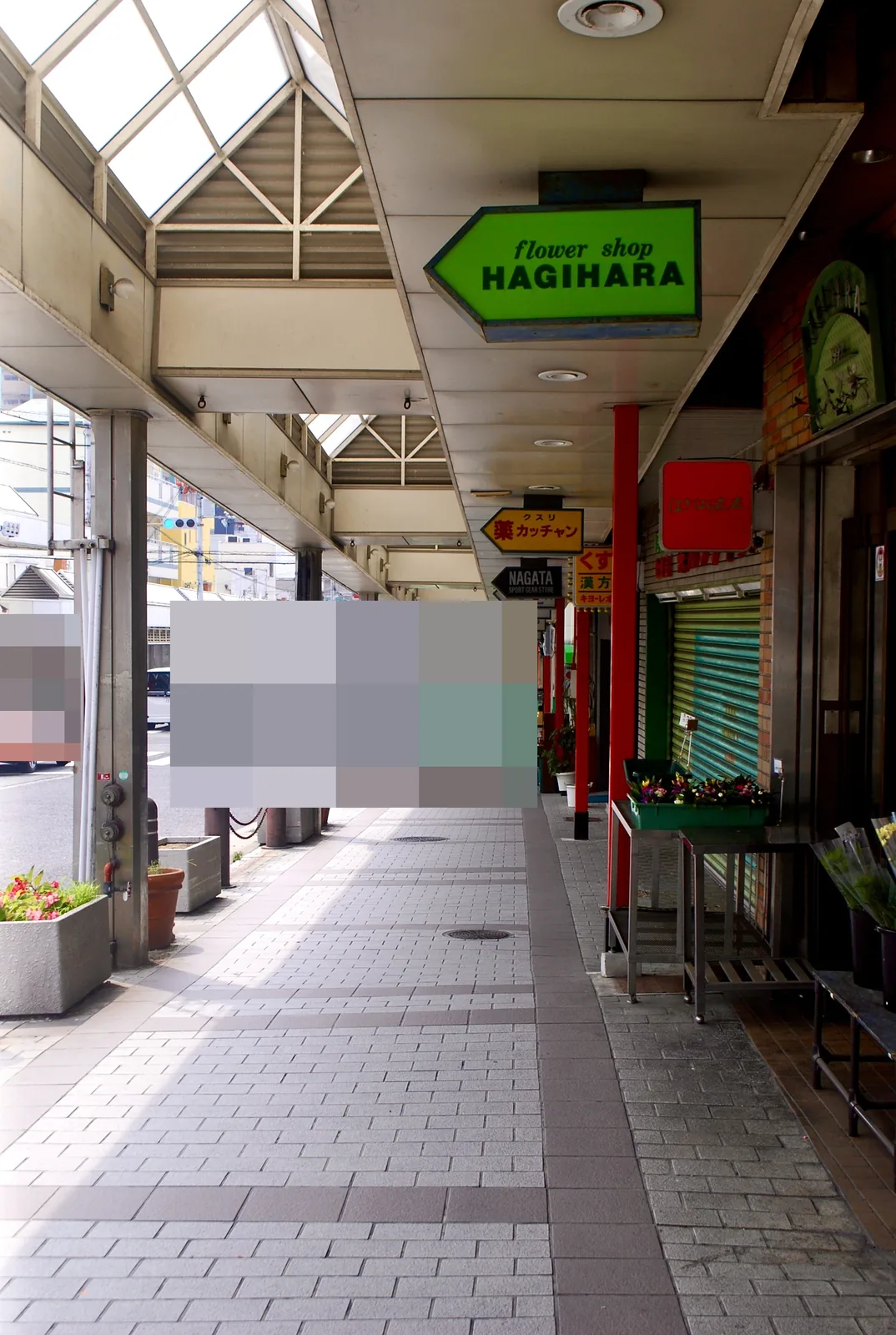 花屋の看板と鉢植えが並ぶ、屋根つきの商店街の歩道