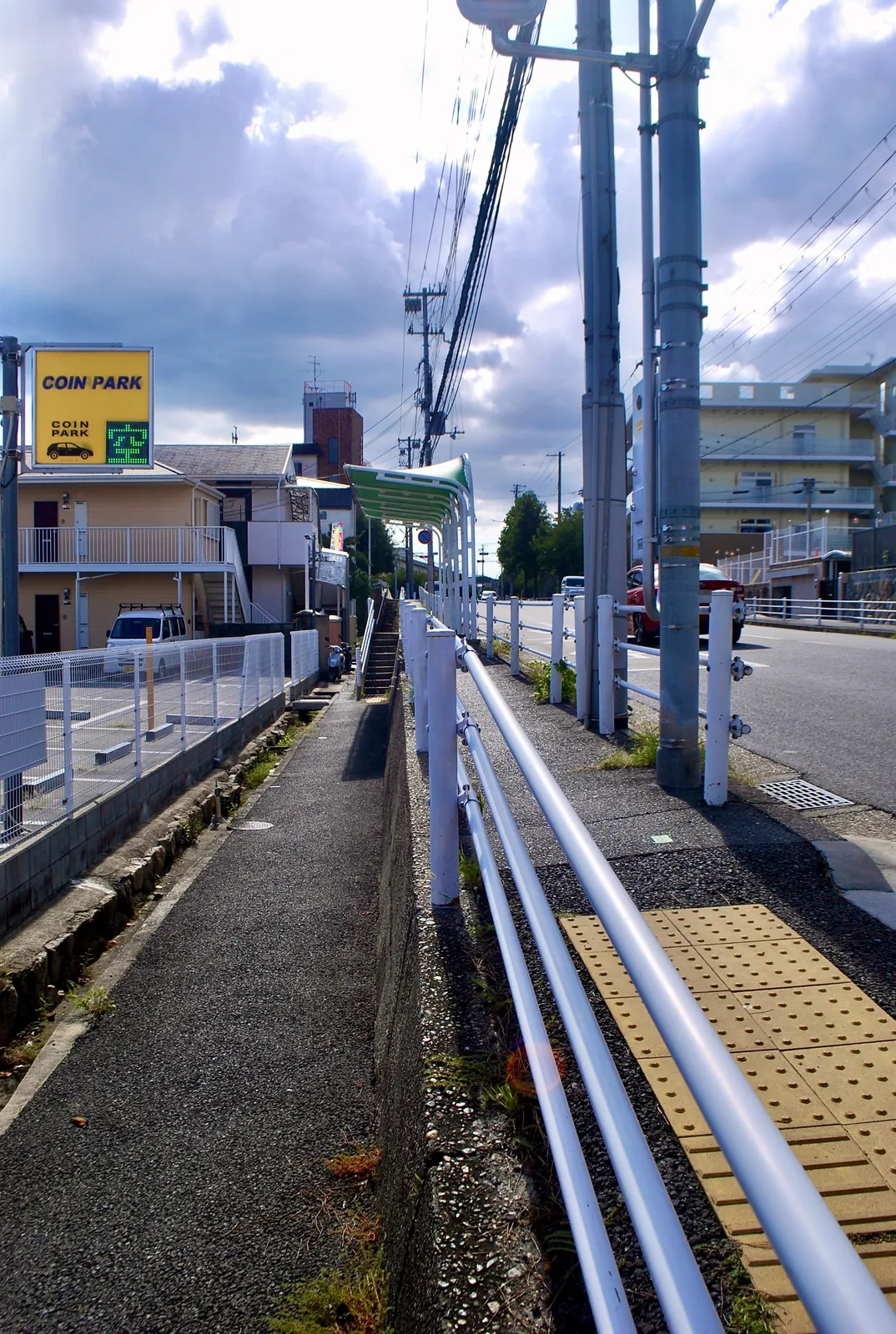 黄色いコインパーキングの看板と、白い柵の続く歩道
