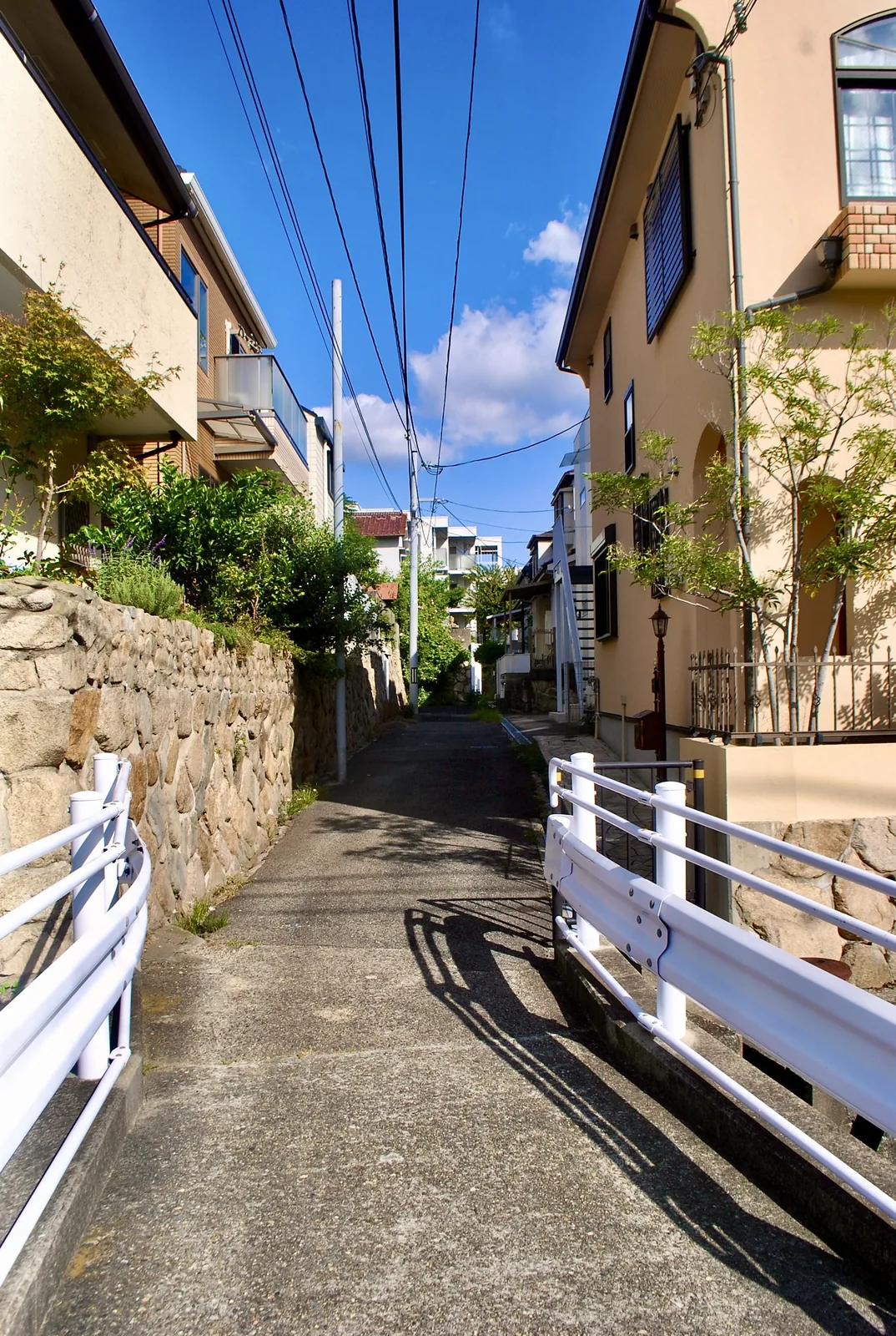 石垣と白いガードレールに挟まれ、青空の下を奥へ続く路地