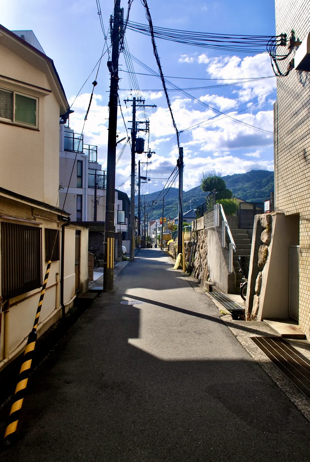 石垣と電柱の並ぶ細い道の先に、六甲の山並みが見える風景