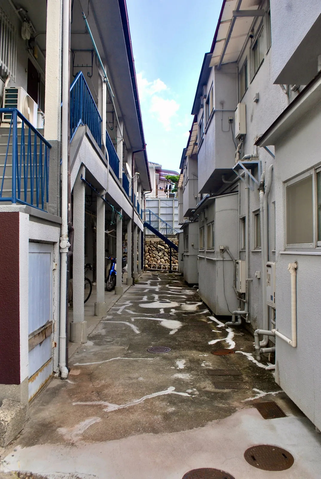 二棟のアパートに挟まれ、奥の石垣と階段へ続く細い路地