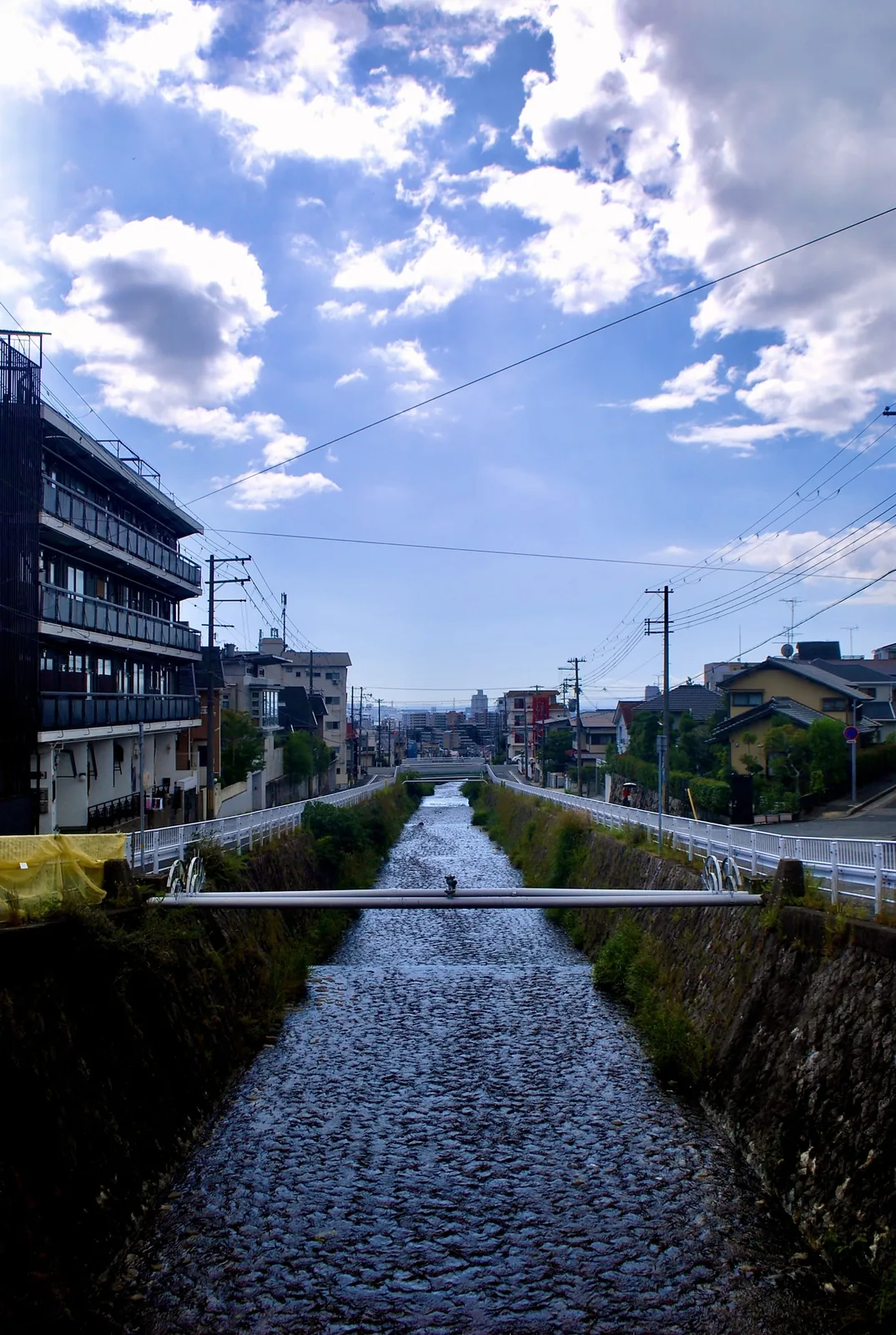 大きな雲の浮かぶ青空の下、町の中をまっすぐ流れる石積みの川