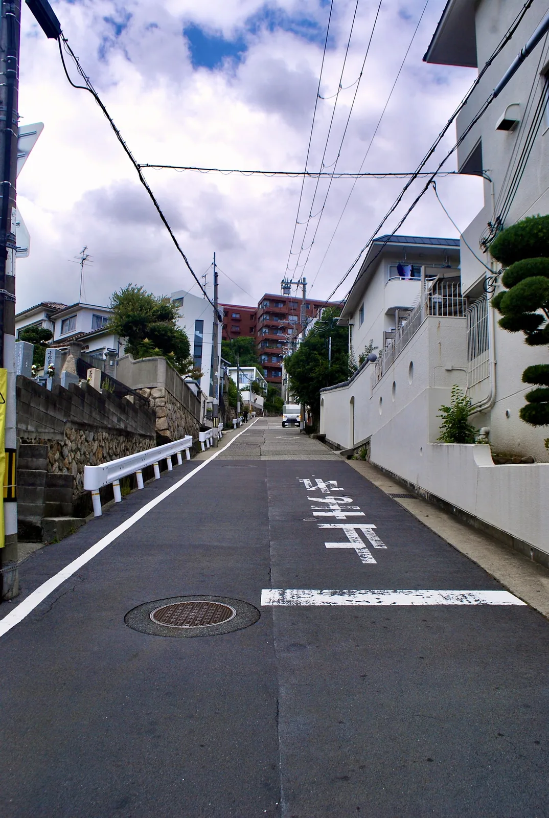 路面に「止まれ」と書かれ、電線の下を奥へ上っていく坂道