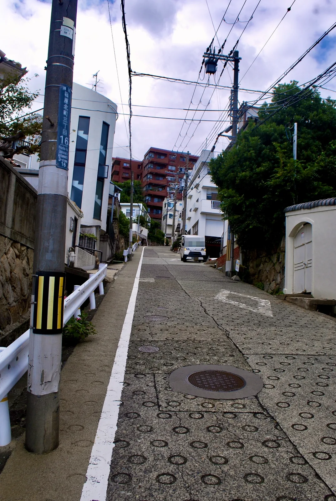 町名表示のある電柱の脇から、丸い滑り止めの模様の坂が上っていく風景