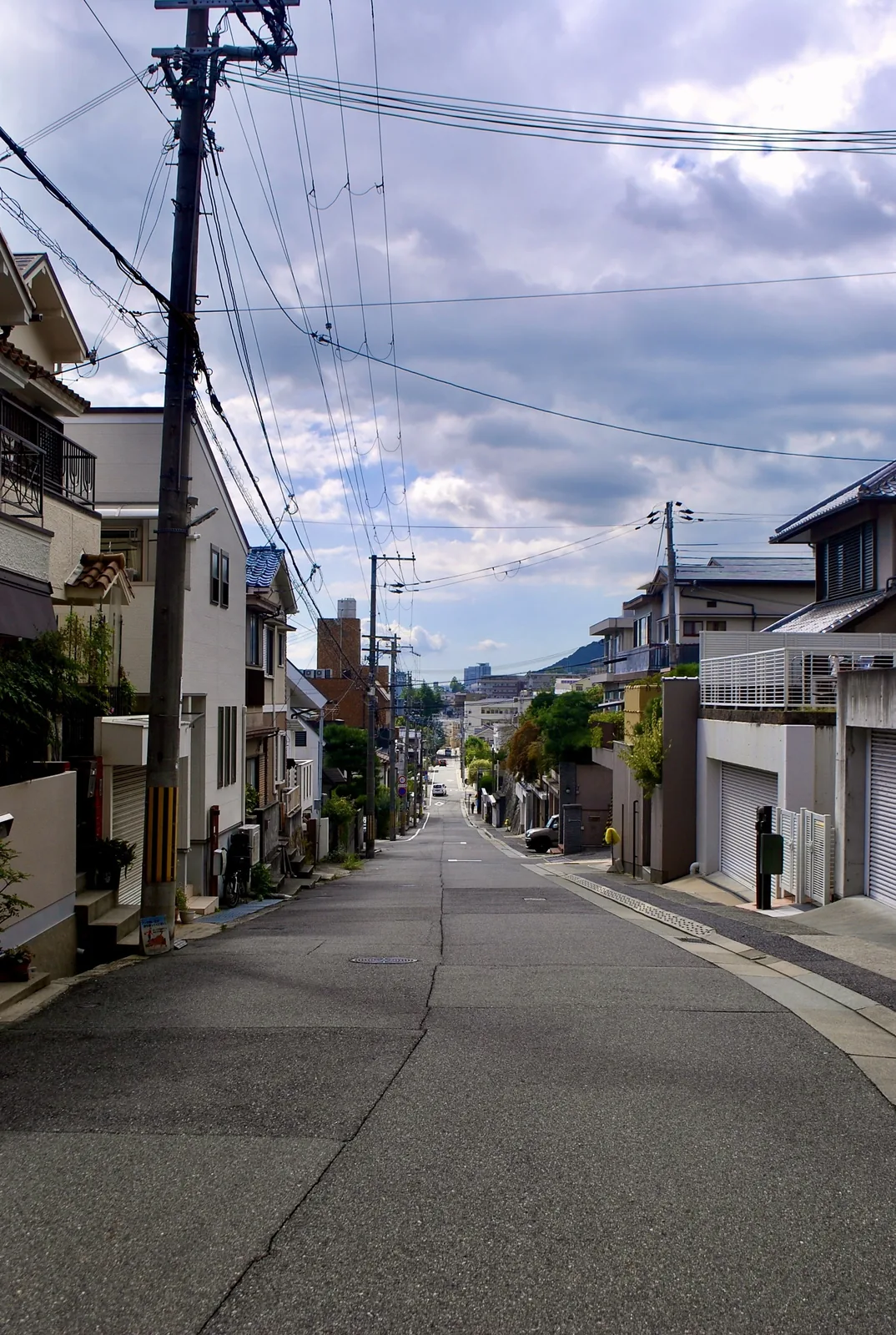 住宅の並ぶ広い坂道が、電線の下を遠くまで下っていく風景