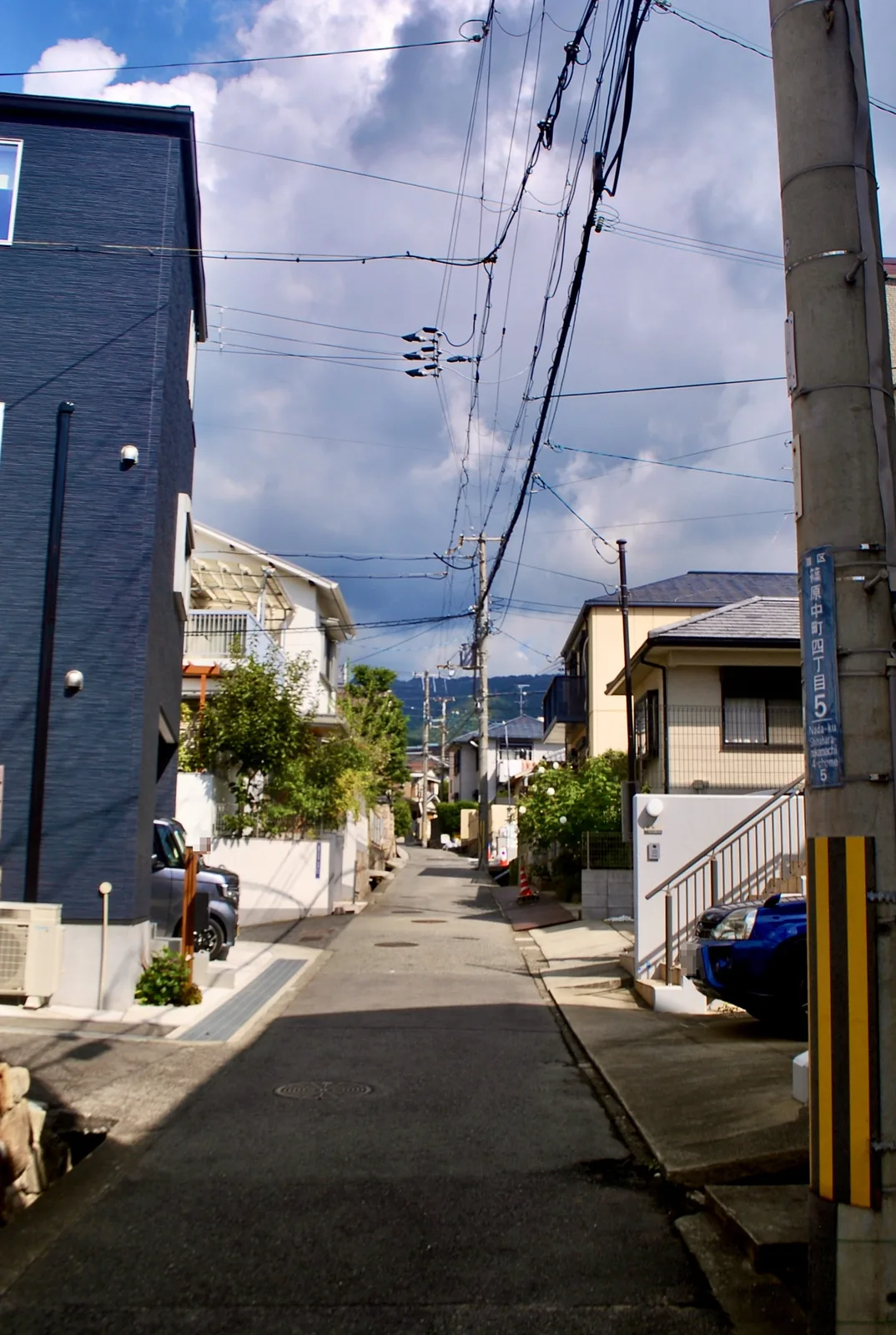 町名表示のある電柱の脇から、奥へ上っていく住宅街の坂道