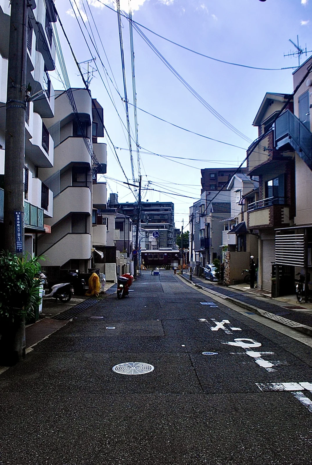 建物に挟まれたまっすぐな通りの奥を、電車が横切る風景