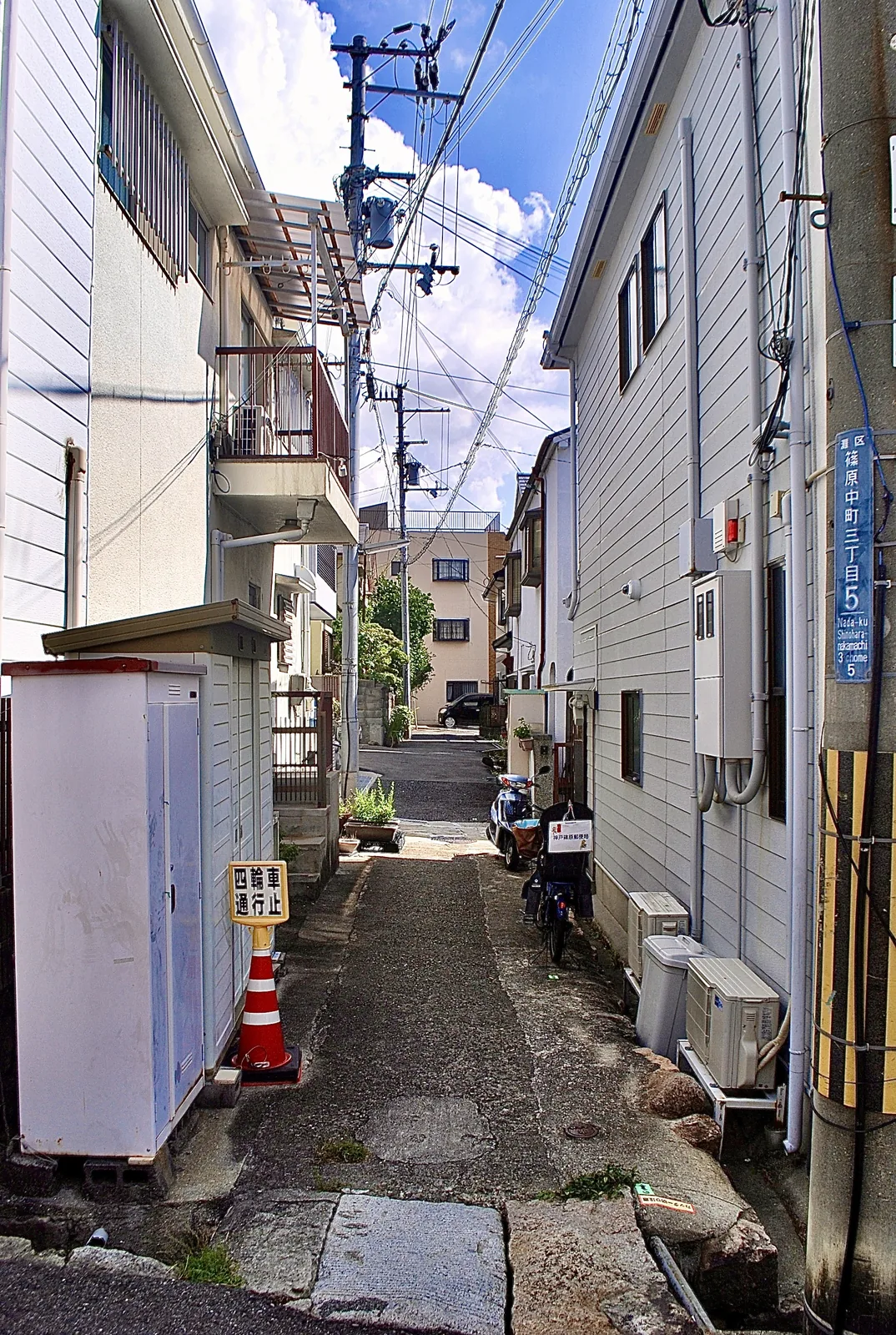 町名表示のある電柱と、家々のあいだを奥へ続く細い路地