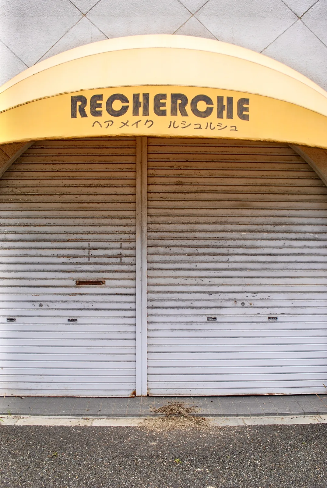 黄色い丸いひさしに「RECHERCHE」の文字がある、シャッターの美容室
