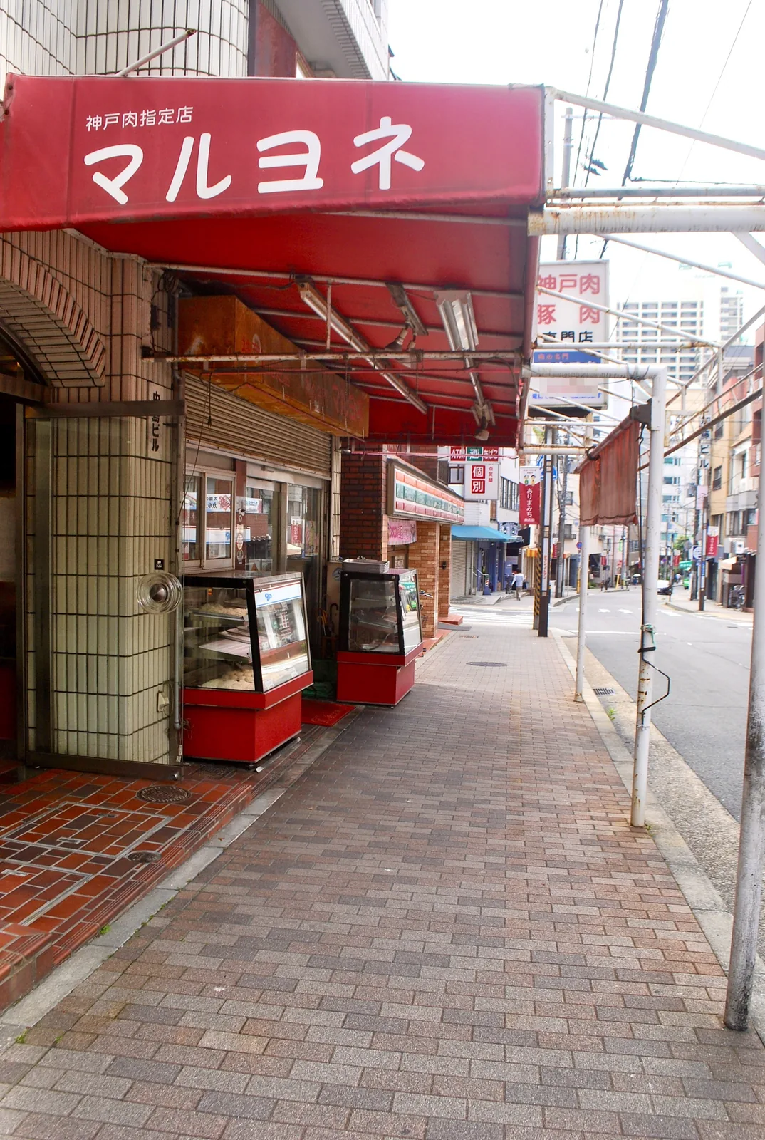 赤い日よけの精肉店の前から、奥へ続く商店街の歩道