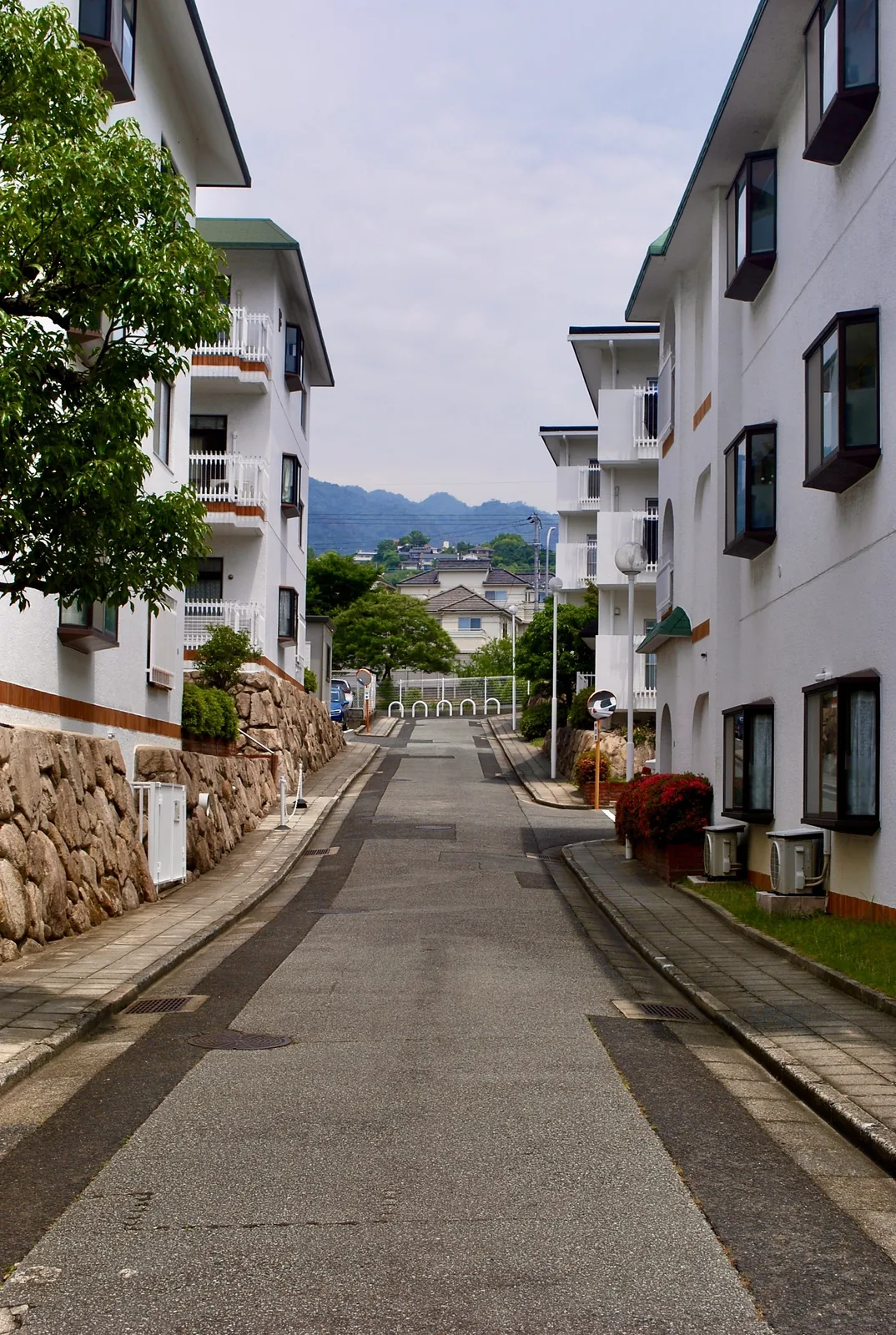 白い建物に挟まれた坂道の先に、山並みが見える風景