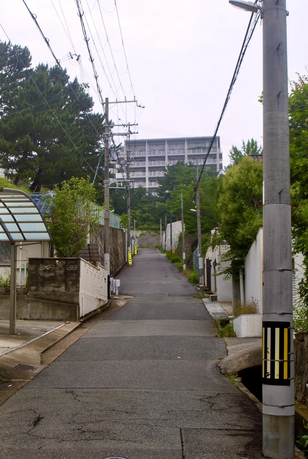電柱の立つ住宅街の上り坂と、その先にそびえるマンション