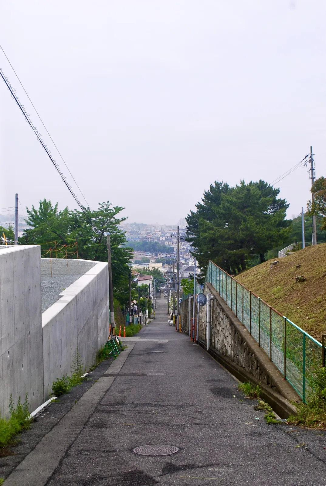 白い擁壁と土手のあいだを、街並みへまっすぐ下る坂道