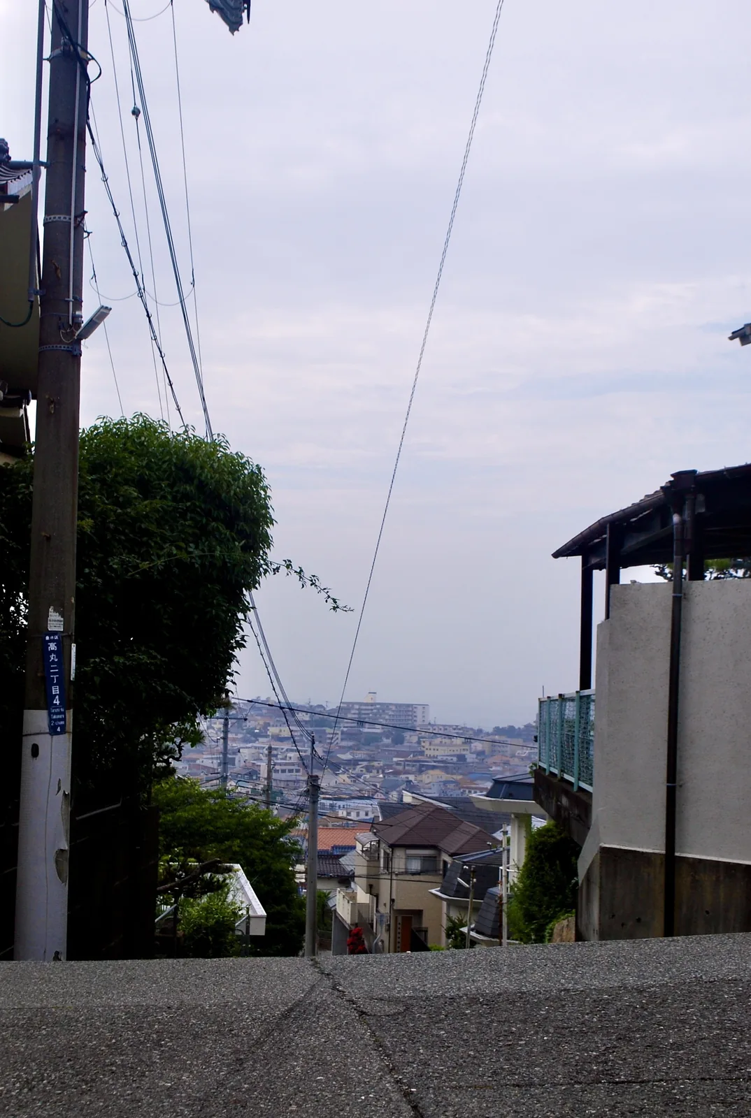 町名表示のある電柱の脇から、遠くの街並みを望む坂の上
