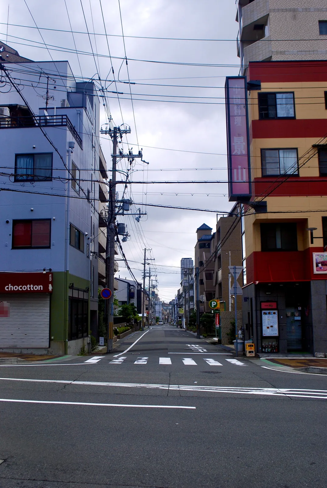 電柱と電線の下、横断歩道の先へまっすぐ続く交差点の風景