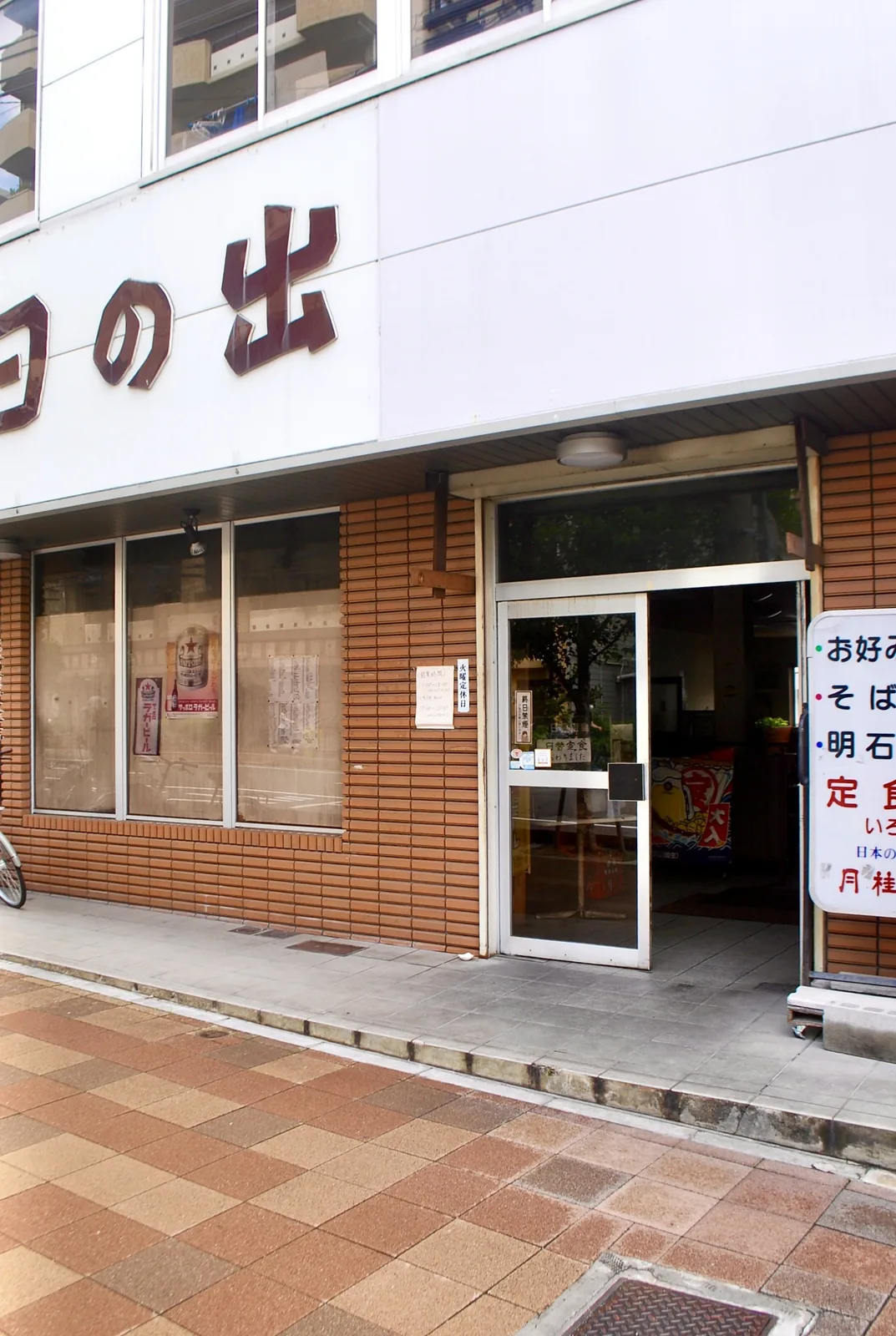 お好み焼・そば・明石焼・定食の看板が出る、レンガタイルの食堂