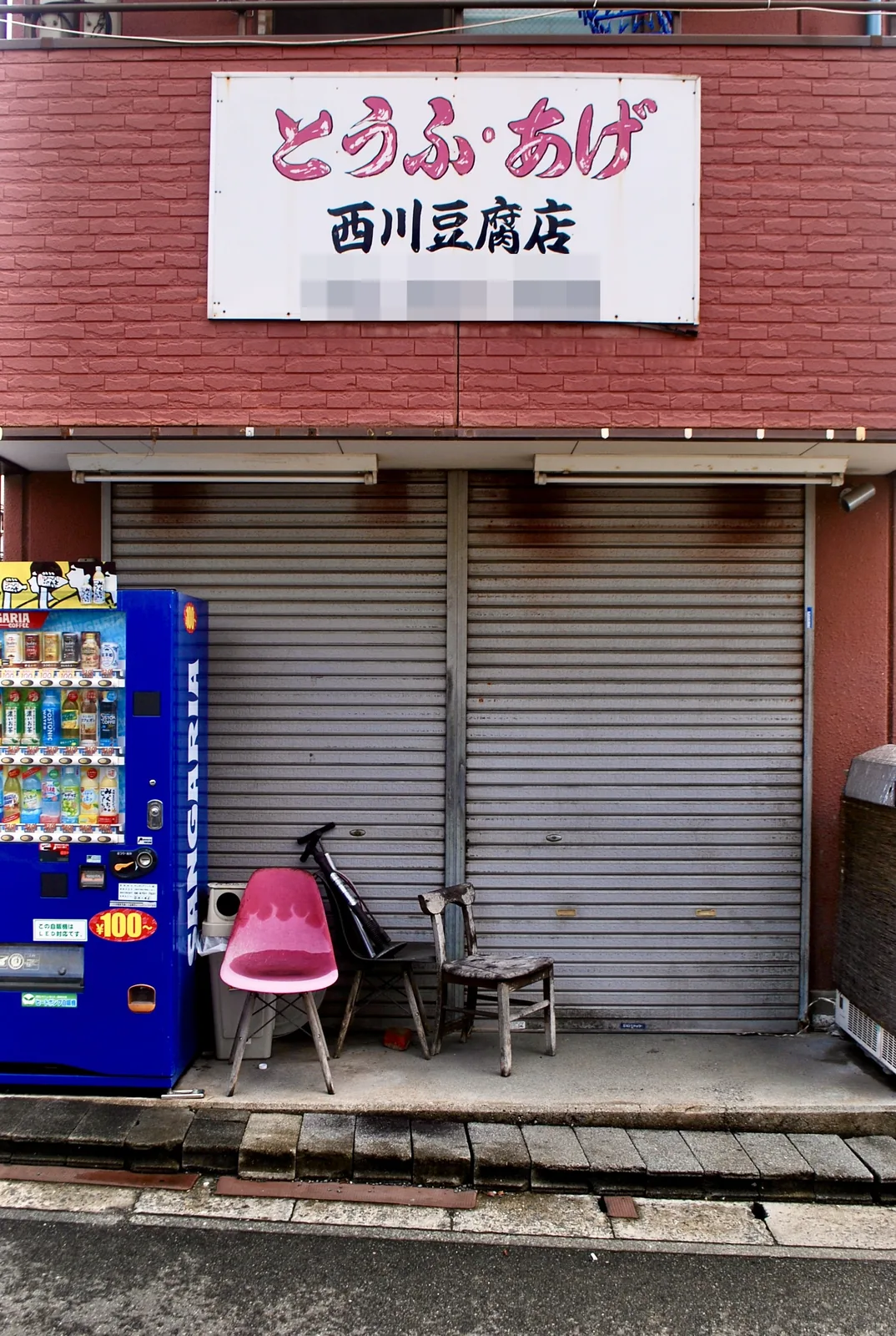 「とうふ・あげ」の看板と自動販売機、ピンクのいすが並ぶ豆腐店の店先