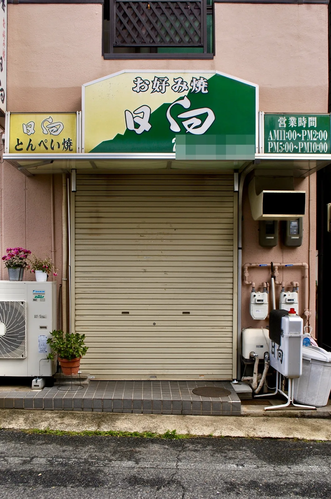 緑の看板の「お好み焼 日向」と、植木鉢の並ぶ店先