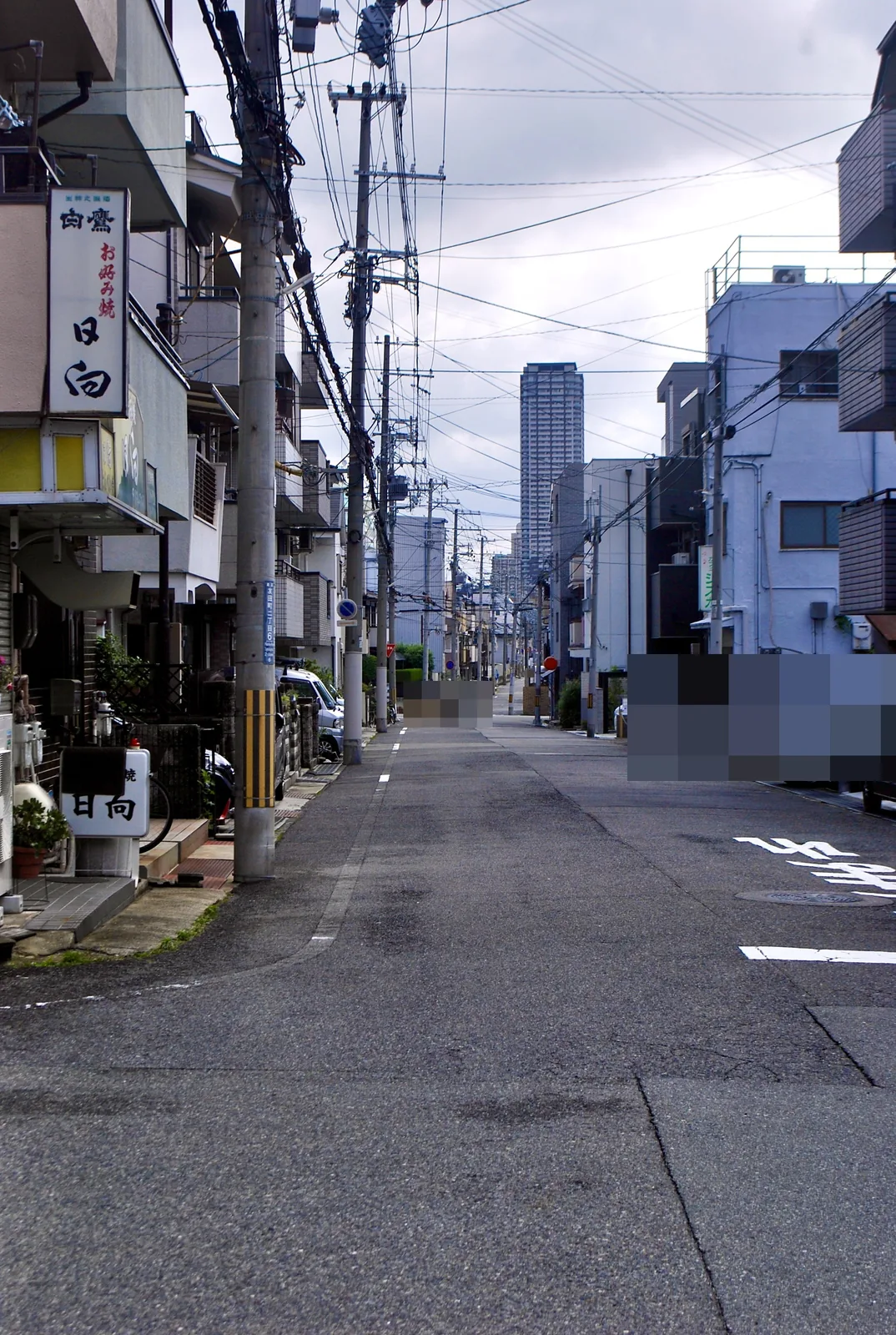 お店の看板の先に、電柱と家々がまっすぐ続く住宅街の道